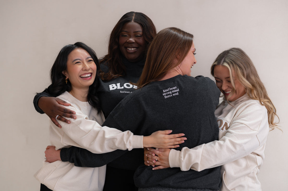 Sisterhood image of four girls hugging wearing Blossom hoodies and sweatshirts from the Original Collection