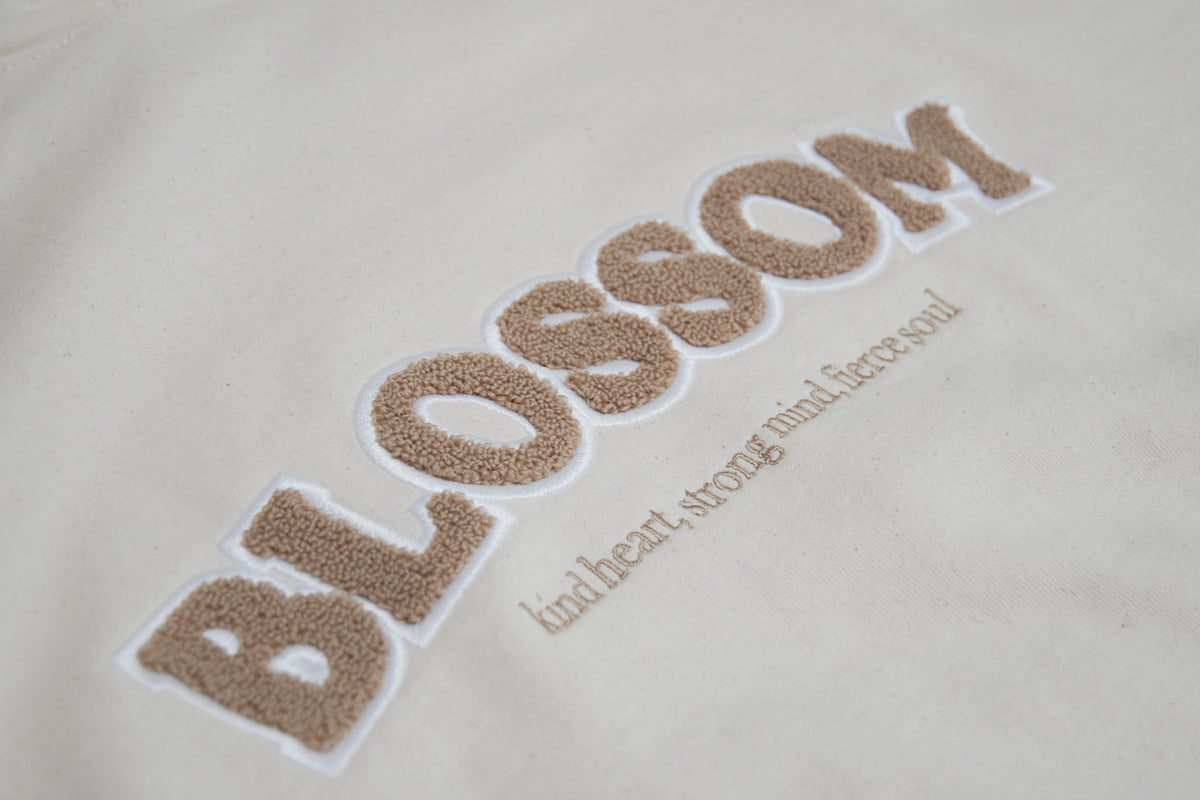 close up of blossom embroidery details featuring the slogan 'kind heart, strong mind, fierce soul'