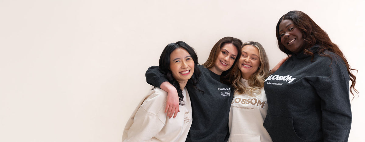 Four women standing together and smiling, wearing matching sweatshirts in black and cream with 'Crossom' branding. The photo is taken against a plain off-white studio background.