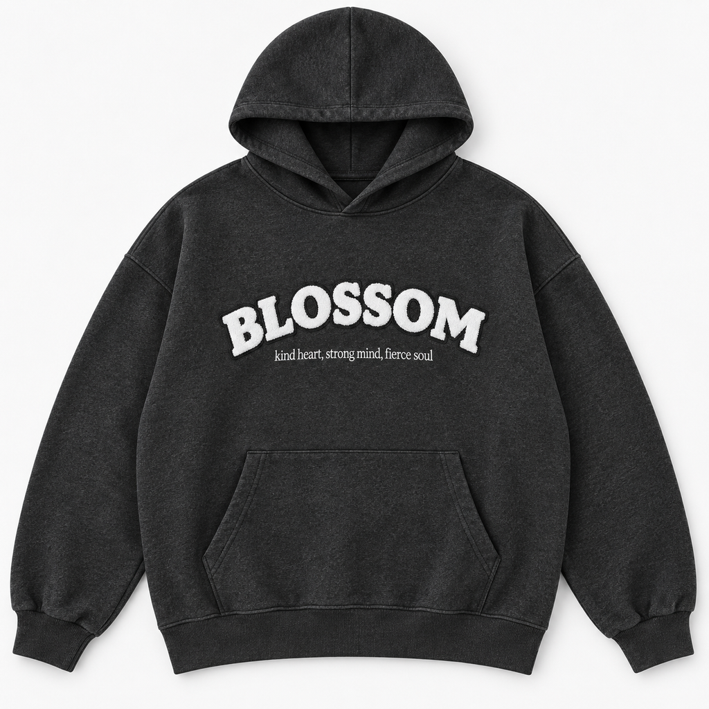 A dark charcoal gray hooded sweatshirt with a white graphic text print reading 'BLOSSOM' and a smaller tagline underneath reading kind heart, strong mind, fierce soul, displayed on a clean white background.