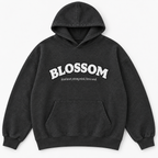 A dark charcoal gray hooded sweatshirt with a white graphic text print reading 'BLOSSOM' and a smaller tagline underneath reading kind heart, strong mind, fierce soul, displayed on a clean white background.