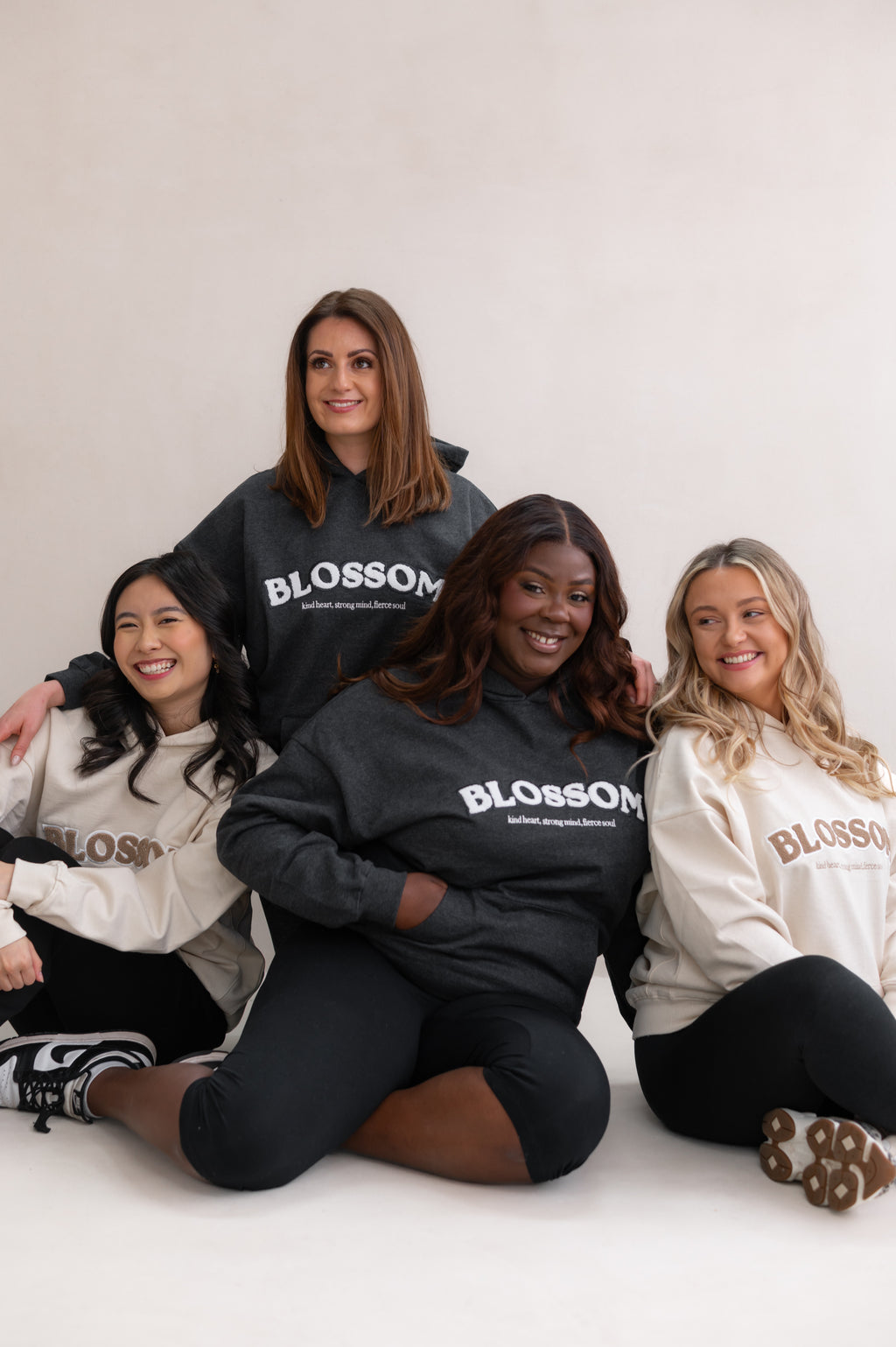Four women wearing 'Blossom' hoodies sitting together on a white background. Sisterhood vibe.