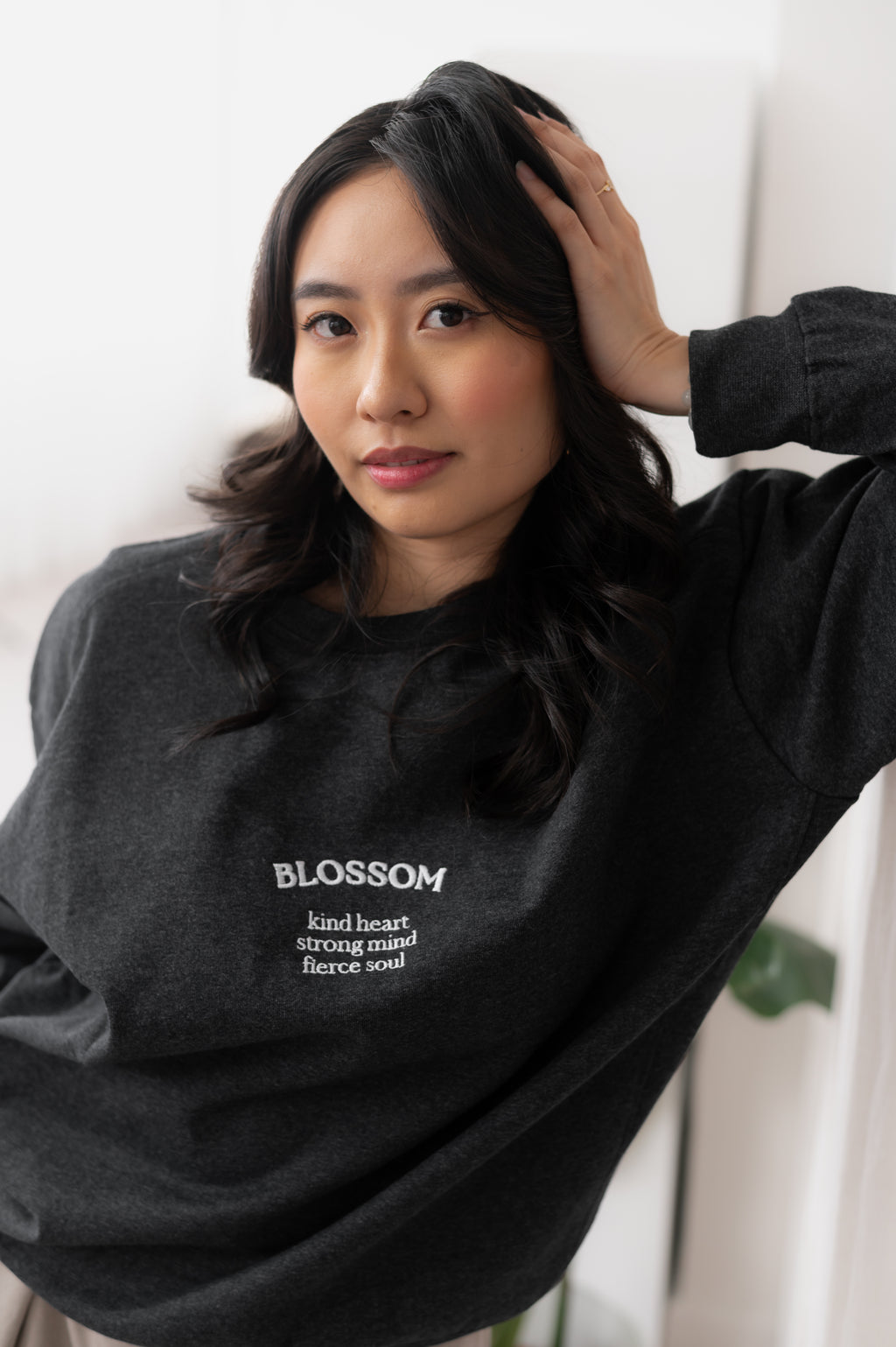 Person wearing a grey sweatshirt with 'Blossom' text, standing indoors.