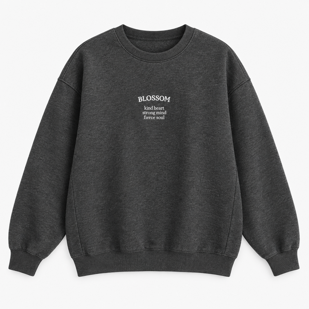 A dark gray heather crewneck sweatshirt with white text on the left chest reading 'BLOSSOM' and a smaller quote underneath that says 'kind heart, strong mind, fierce soul', displayed on a clean white background.
