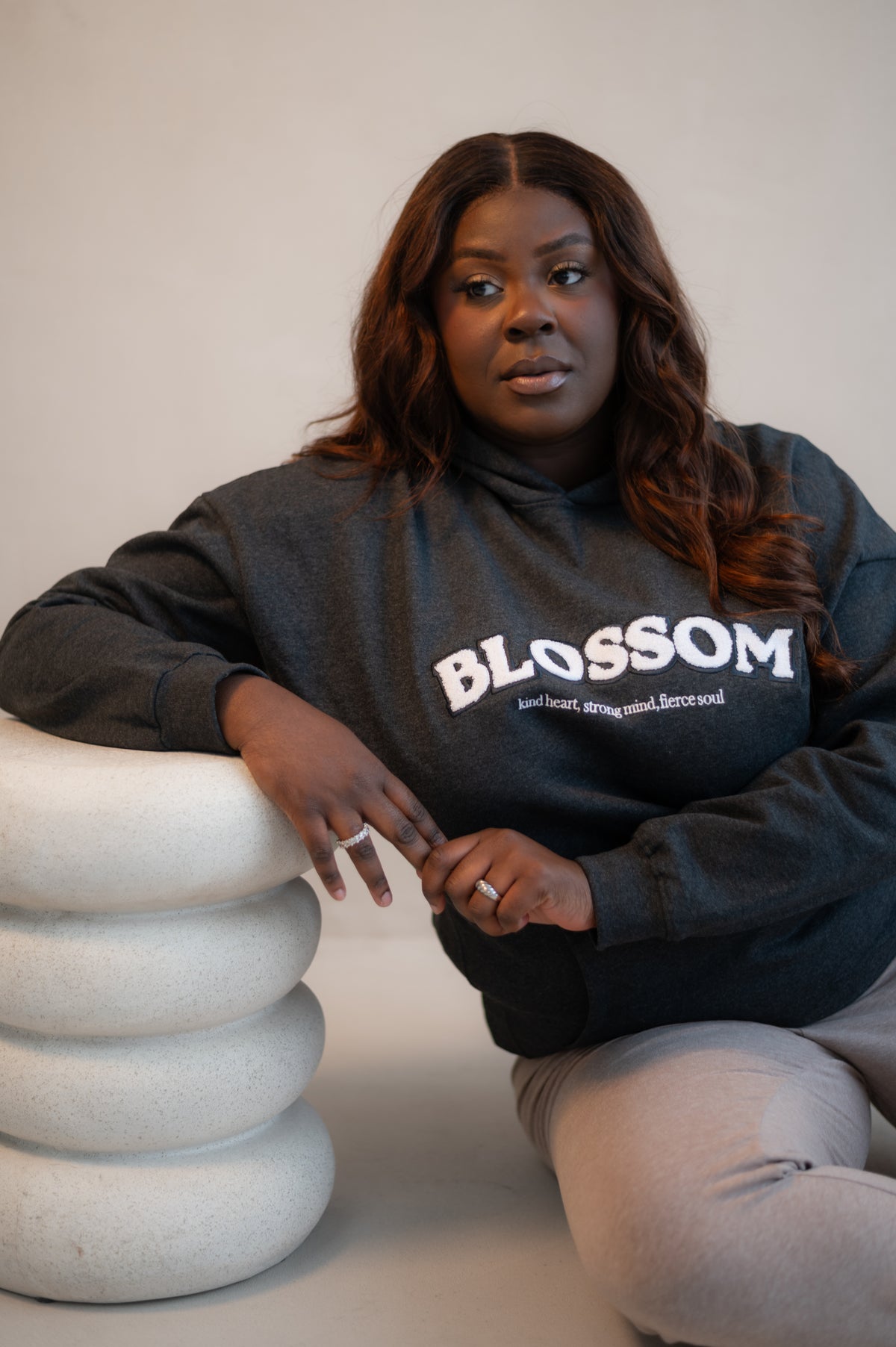 Person wearing a shadow grey hoodie with 'Blossom' text, sitting on a white surface.